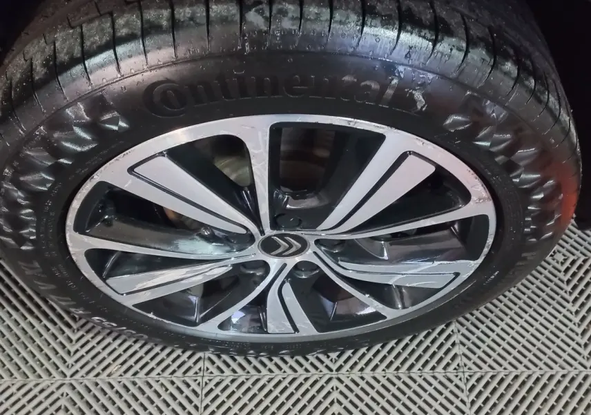 Gros plan sur la jante alliage noire et argentée avec logo Citroën, pneu Continental humide, sol en grille plastique.