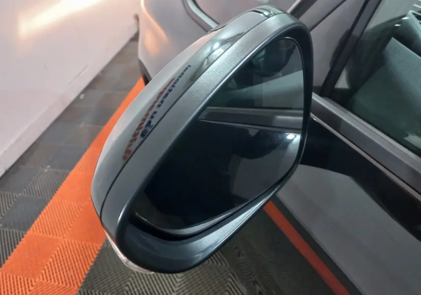Rétroviseur extérieur droit gris métallisé du Citroën Grand C4 Spacetourer, vue rapprochée sur fond de sol noir et orange.