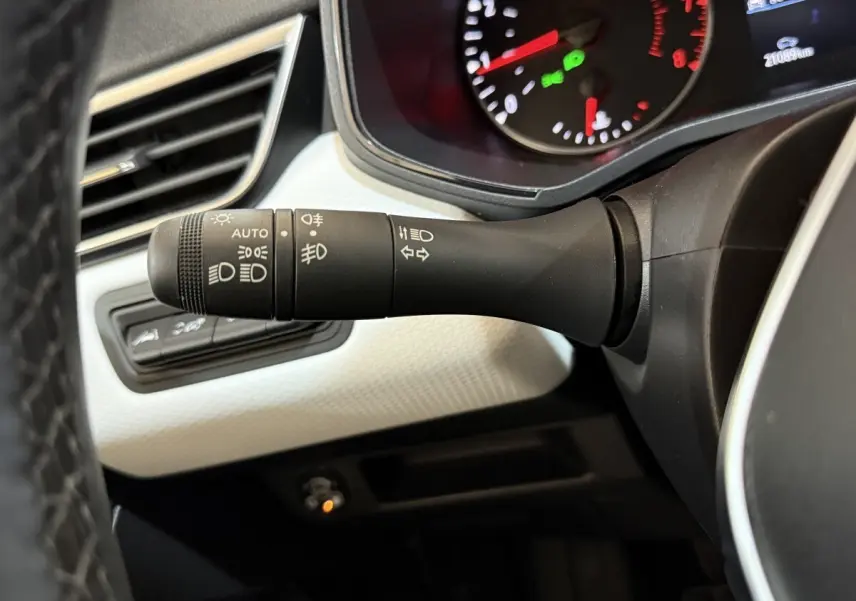 Gros plan sur la manette des phares et clignotants à gauche du volant dans l’habitacle blanc et noir d’une Renault Clio Business 2022.