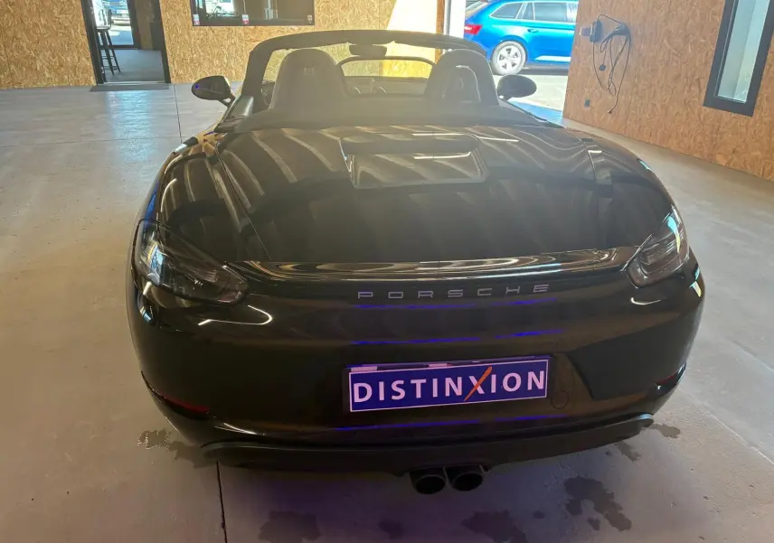 Vue arrière d'une Porsche 718 Boxster noire cabriolet, avec capote baissée et double sortie d'échappement centrale.