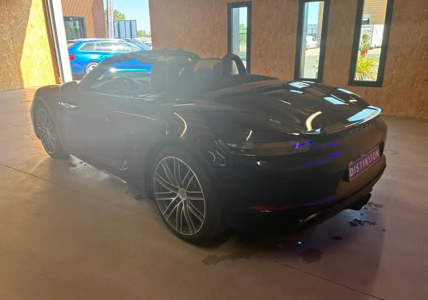 Vue 3/4 arrière droite d'une Porsche 718 Boxster noire cabriolet, avec jantes alliage et intérieur visible en alcantara noir.