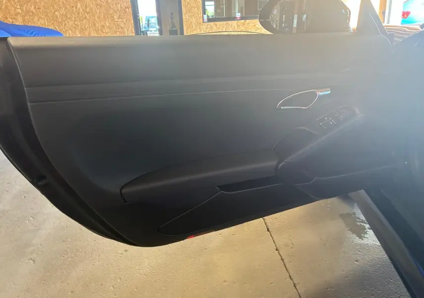 Vue rapprochée de la porte intérieure côté gauche noire d’une Porsche 718 Boxster 2018 avec poignée chromée et commandes électriques.