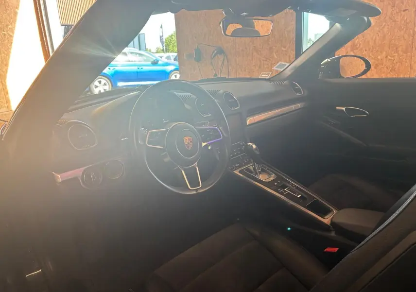 Intérieur noir de la Porsche 718 Boxster 2.0 300 vue côté conducteur, mettant en valeur le volant et la console centrale.