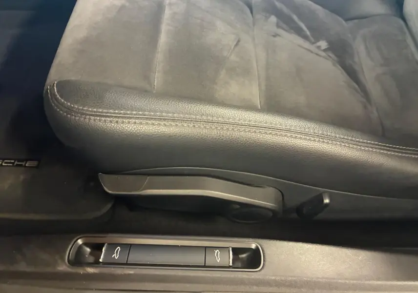 Gros plan sur le siège avant gauche en cuir noir et les commandes d'ouverture du coffre et du capot d'une Porsche 718 Boxster noire.