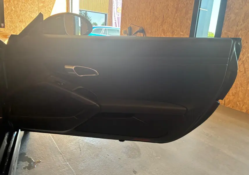 Vue intérieure de la porte côté gauche noire de la Porsche 718 Boxster 2.0 300 essence, avec poignée argentée.