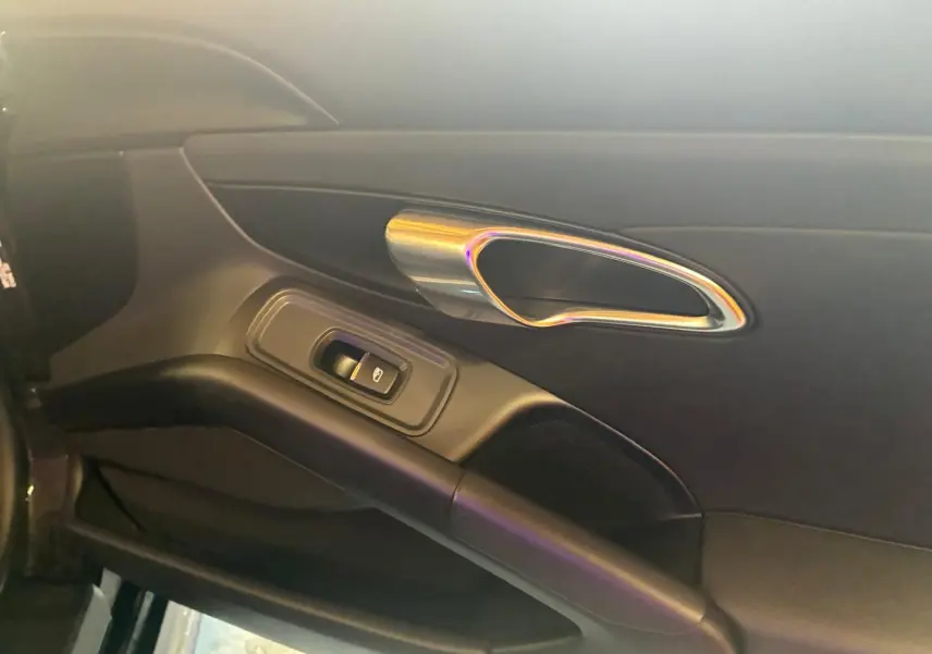 Vue rapprochée de la porte intérieure côté gauche noire du Porsche 718 Boxster 2018 avec poignée chromée et commande de vitre.