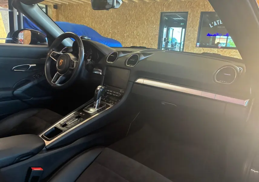 Intérieur noir de la Porsche 718 Boxster 2.0 300, vue côté conducteur, avec volant sport et console centrale automatique.