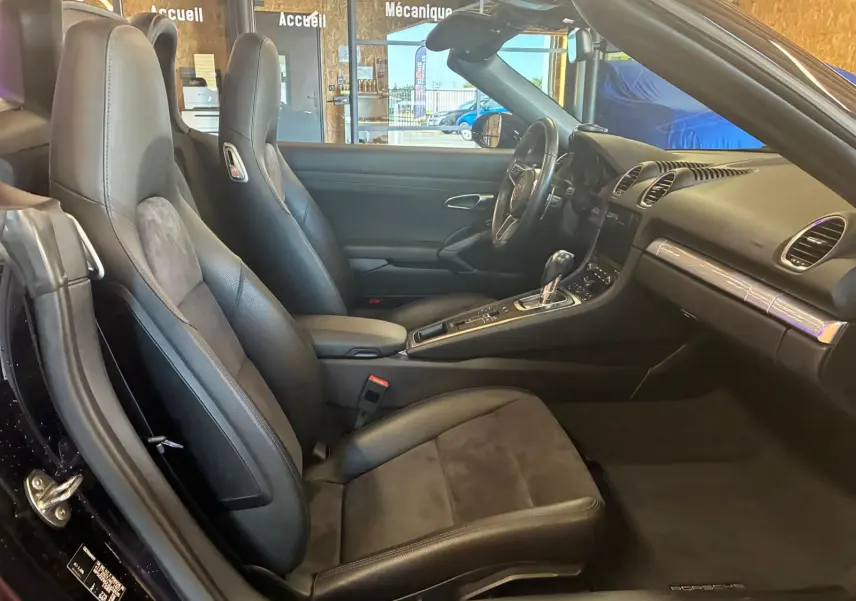 Vue intérieure côté gauche de la Porsche 718 Boxster noire, mettant en valeur les sièges sport en cuir et alcantara et la console centrale.