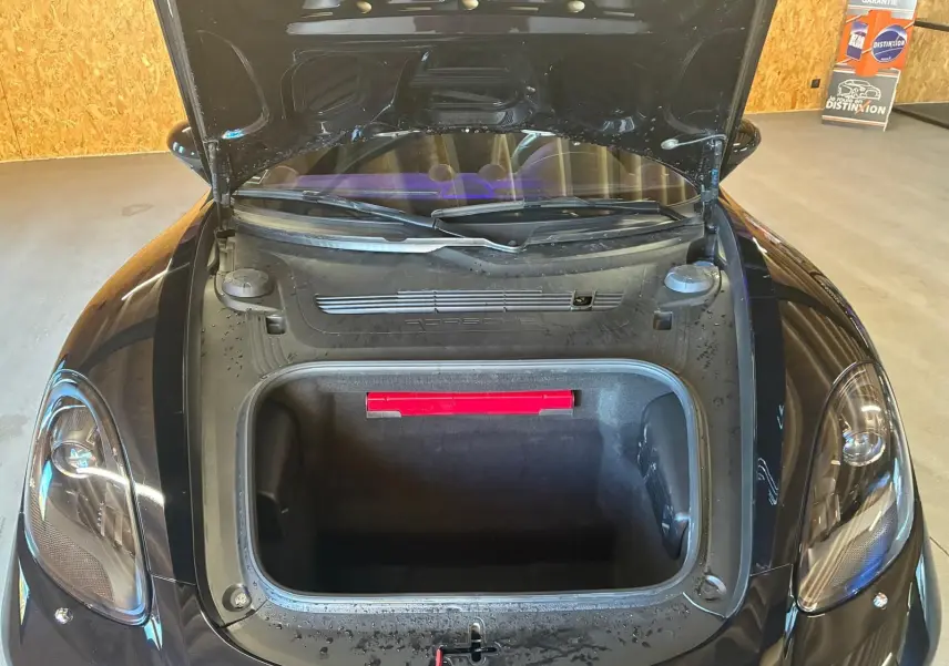 Vue plongeante avant du coffre ouvert d'une Porsche 718 Boxster noire, mettant en valeur l'espace de rangement avant.