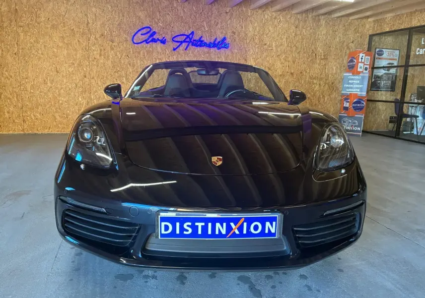 Vue frontale d'une Porsche 718 Boxster noire 2018, capote ouverte, avec logo Porsche visible sur le capot.