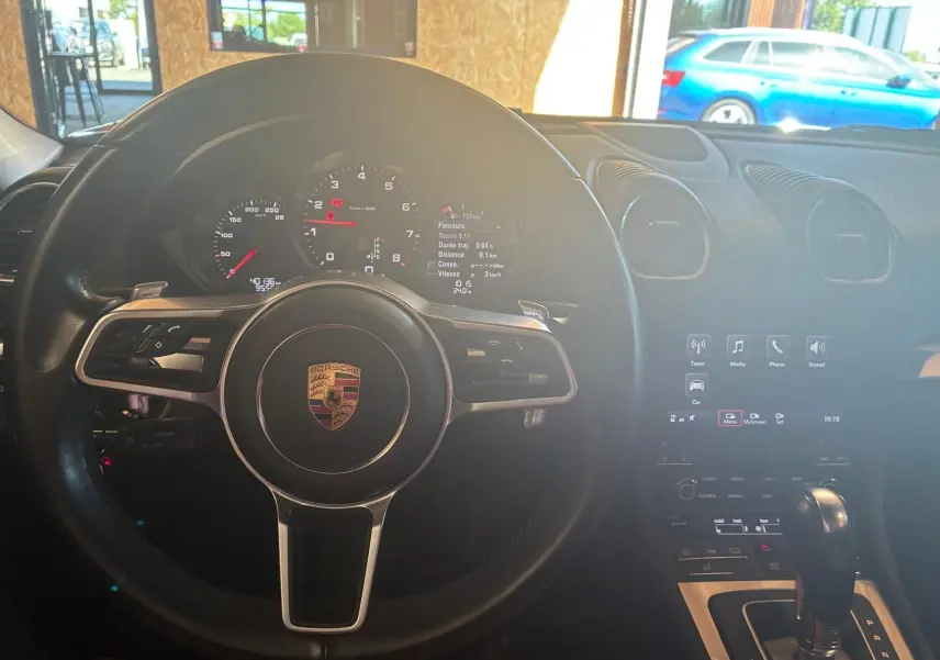 Vue intérieure centrée sur le volant noir de la Porsche 718 Boxster 2.0 300 de 2018 avec tableau de bord et console centrale visibles.