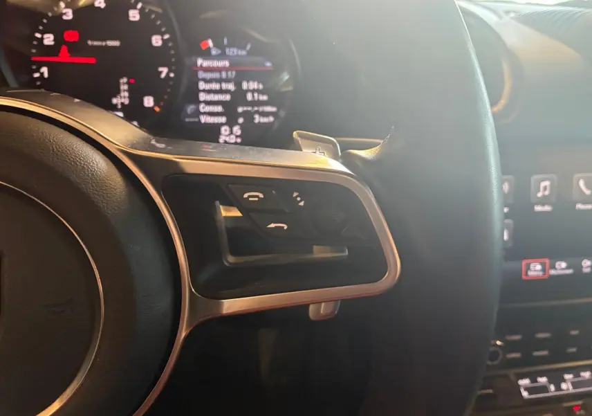 Vue rapprochée du côté gauche du volant noir de la Porsche 718 Boxster 2018 avec commandes intégrées et tableau de bord lumineux.
