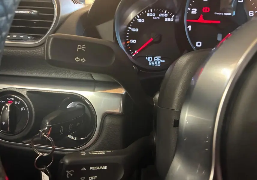 Gros plan sur le tableau de bord noir de la Porsche 718 Boxster 2.0 300, avec compteur et clé insérée.