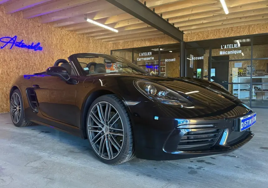 Vue 3/4 avant droite d'une Porsche 718 Boxster 2.0 300 noire cabriolet, avec jantes alliage et intérieur visible.
