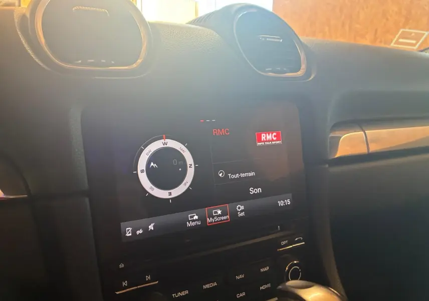 Vue rapprochée de l’écran tactile central du Porsche 718 Boxster noir, affichant la boussole et la radio RMC.