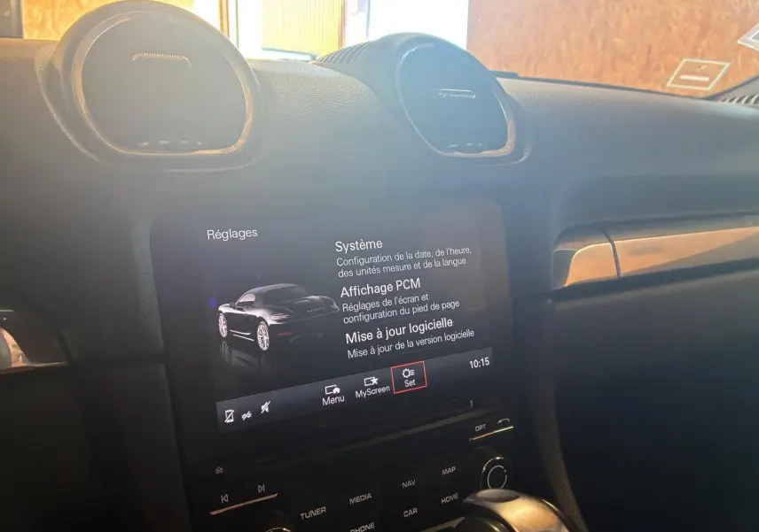 Vue intérieure du tableau de bord de la Porsche 718 Boxster noire, avec écran tactile affichant les réglages système.
