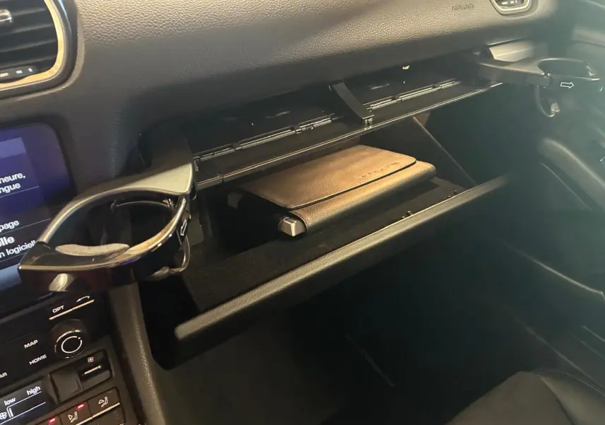 Vue intérieure côté passager du coffre à gants ouvert d'une Porsche 718 Boxster noire avec un porte-gobelet déployé.