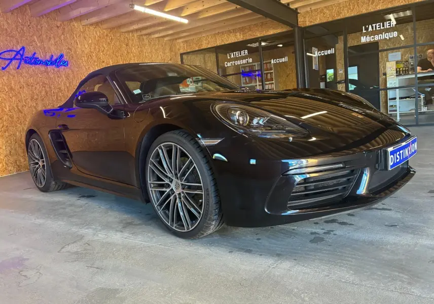 Porsche 718 Boxster noir vue 3/4 avant droit, avec jantes multibranches et phares LED dans un garage.