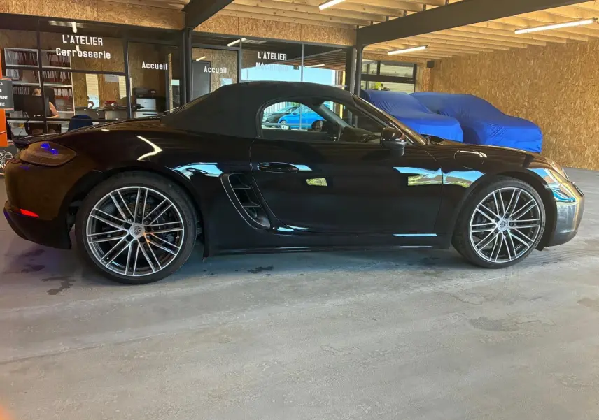 Vue latérale gauche d'une Porsche 718 Boxster noire de 2018 avec toit souple et jantes alliage multibranches.