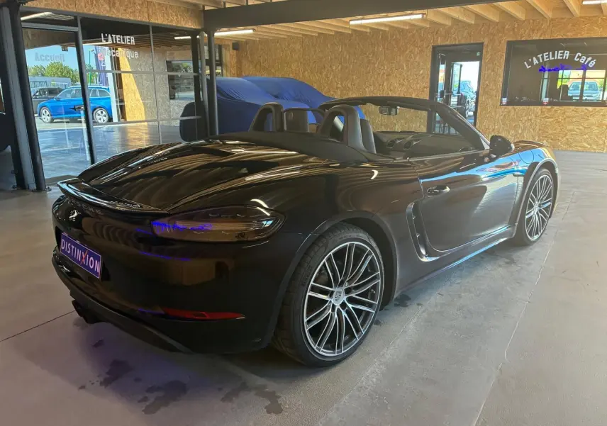 Vue 3/4 arrière droite d'une Porsche 718 Boxster noire cabriolet avec jantes alliage et intérieur ouvert.