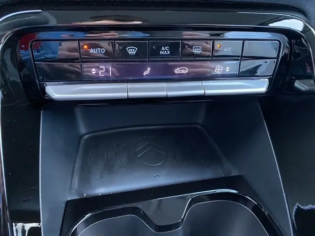 Vue rapprochée du panneau de commande de la climatisation et de la zone de recharge à induction noire dans une Citroën C3 Aircross gris foncé.