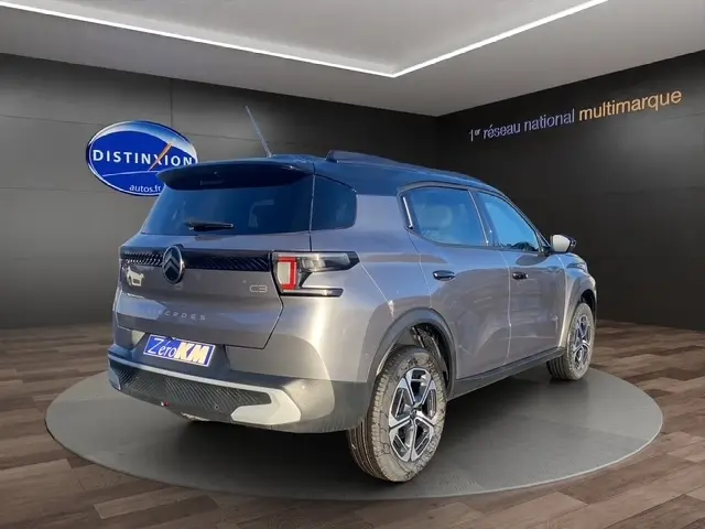Vue 3/4 arrière droite d'une Citroën C3 Aircross hybride gris foncé avec jantes distinctives et toit noir en showroom.