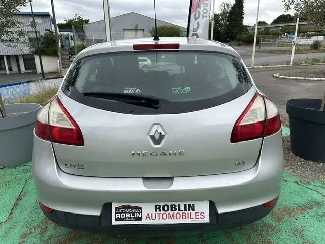 Vue arrière d'une Renault Mégane 3 gris clair, avec logo et badges visibles sur un parking extérieur.