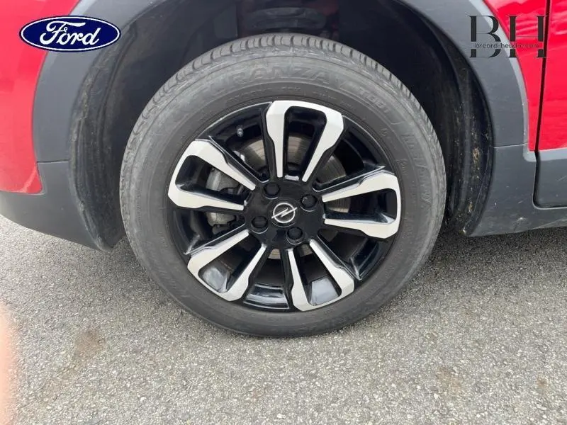 Gros plan sur la roue avant gauche de l'Opel Crossland rouge Kardio métallisé avec jante alu bicolore distinctive.