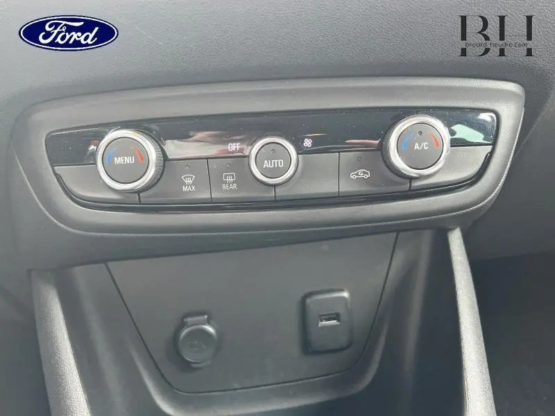 Panneau de commande de climatisation automatique d'un Opel Crossland rouge, avec boutons rotatifs et prises USB et 12V en dessous.