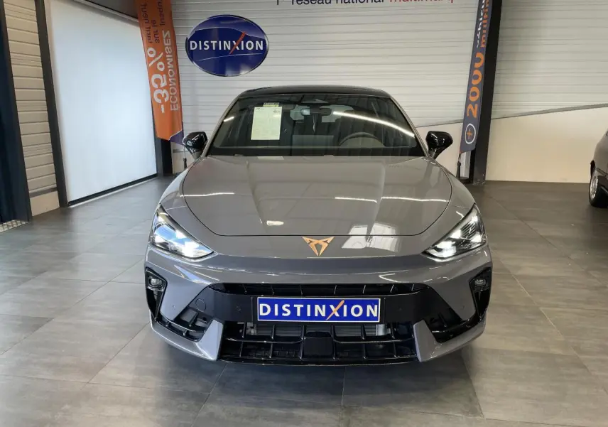Vue avant d'une CUPRA Leon gris Graphène avec logo cuivré et phares LED allumés en showroom.