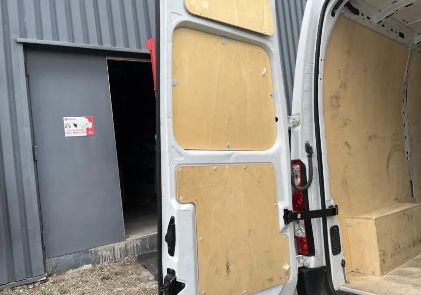 Vue arrière porte ouverte du Renault Master blanc avec habillage bois intérieur et protection latérale complète.