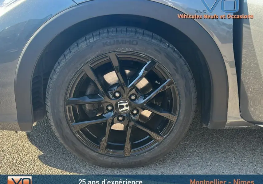 Gros plan sur la jante alliage noire côté gauche d'une Honda Civic gris 2015 avec logo Honda au centre.
