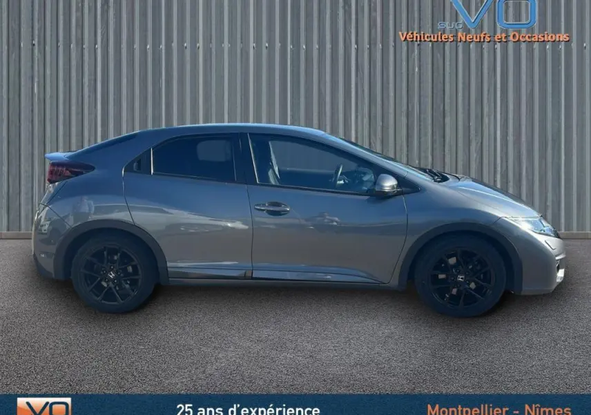 Profil côté gauche d'une Honda Civic gris 2015 avec jantes alliage noires et vitres surteintées sur fond industriel.
