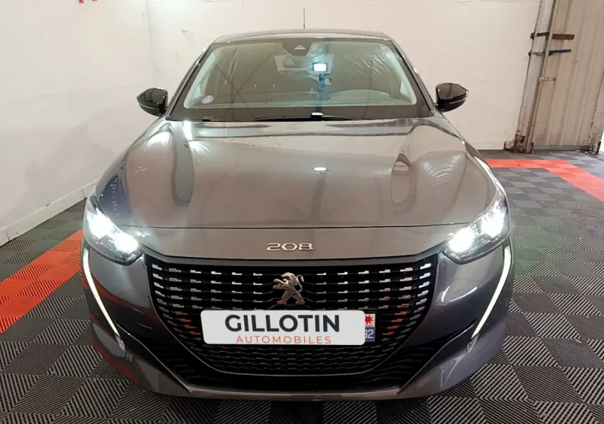 Vue frontale d'une Peugeot 208 gris foncé avec phares LED allumés et calandre noire distinctive.