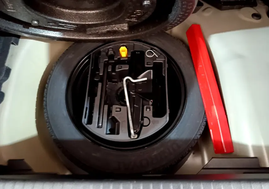 Vue plongeante sur la roue de secours et le kit d'outils dans le coffre d'une Peugeot 208 gris foncé 2022.