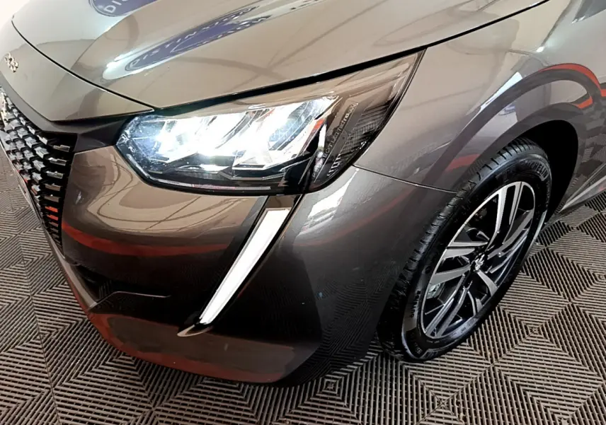 Gros plan sur l'avant droit d'une Peugeot 208 gris foncé 2022, mettant en valeur le phare LED et la jante alliage.