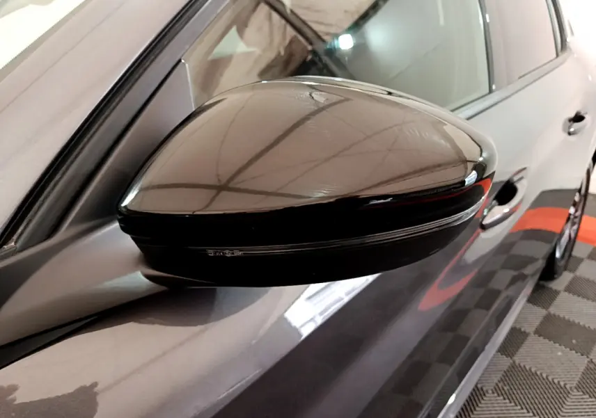 Rétroviseur noir côté gauche d'une Peugeot 208 gris foncé, vue rapprochée sur la portière avant.