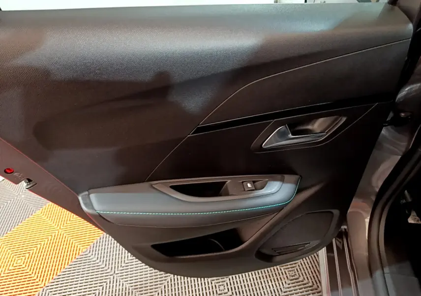 Vue intérieure de la porte avant droite gris foncé de la Peugeot 208 PureTech 100 Allure Pack avec surpiqûres bleues.