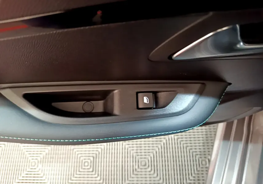 Poignée intérieure de porte côté gauche avec bouton de verrouillage sur Peugeot 208 gris foncé, vue rapprochée.