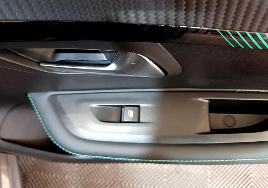 Gros plan sur la poignée intérieure côté gauche de la porte d'une Peugeot 208 gris foncé avec surpiqûres bleues.