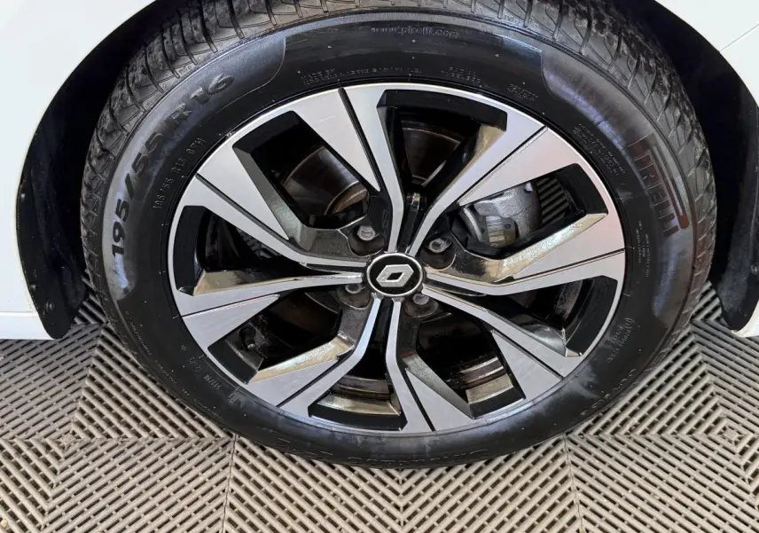 Gros plan sur la roue avant droite d'une Renault Clio blanche avec jante alliage bicolore et logo central Renault.