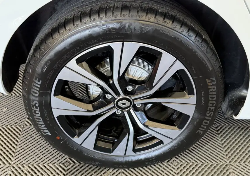Gros plan sur la roue avant droite d'une Renault Clio blanche 2023 avec jante alliage bicolore et pneu Bridgestone.