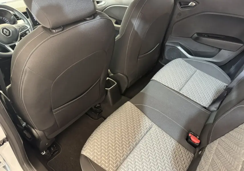 Vue intérieure arrière côté droit de la Renault Clio blanche 2023, montrant les sièges tissu bicolores et le tableau de bord partiel.