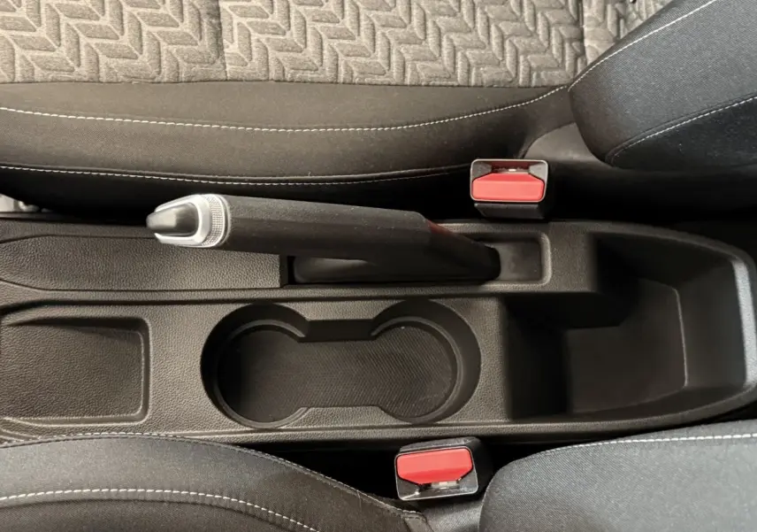 Vue plongeante sur le frein à main manuel et porte-gobelets entre les sièges noirs de la Renault Clio Business blanche.