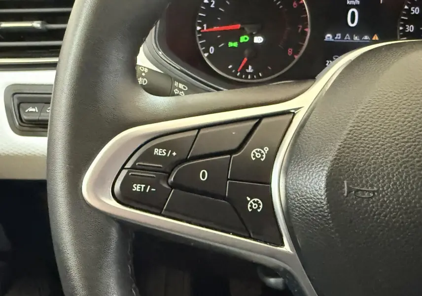 Gros plan sur le volant noir de la Renault Clio 2023 avec commandes du régulateur de vitesse et tableau de bord partiel.