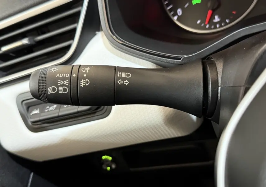 Gros plan sur la commande des phares et clignotants à gauche du volant, tableau de bord blanc texturé en arrière-plan.