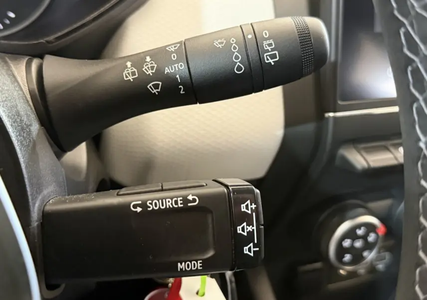 Gros plan sur les commandes au volant noir de la Renault Clio Business TCe 100 GPL, avec tableau de bord partiellement visible.