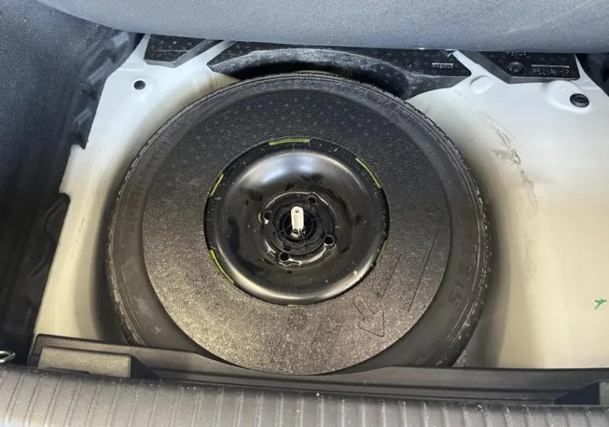 Roue de secours noire dans le coffre blanc du DS3 Crossback 2022 vue en plongée, sans autres éléments visibles.