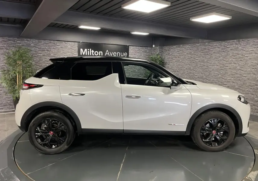 Vue de profil côté gauche d'un DS3 Crossback 2022 bi-ton blanc et noir avec jantes noires en intérieur showroom.