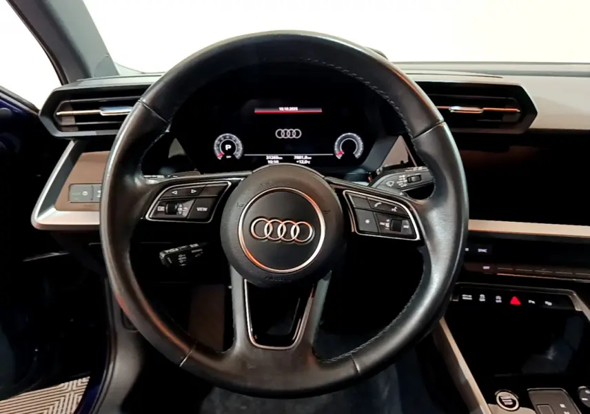 Vue centrée sur le volant cuir noir et le tableau de bord numérique de l'Audi A3 35 TFSI bleu 2023.
